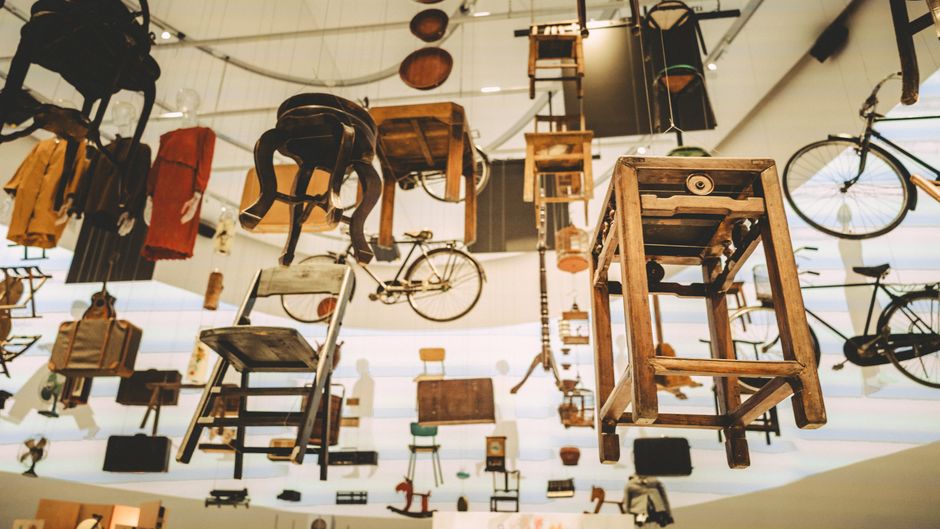 Unique art installation of vintage furniture and bicycles suspended in mid-air at an exhibition.